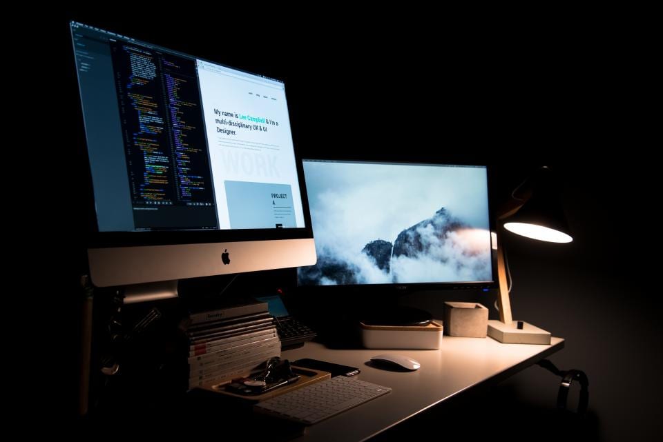 A dual-monitor desk setup with both screens on arms at eye level