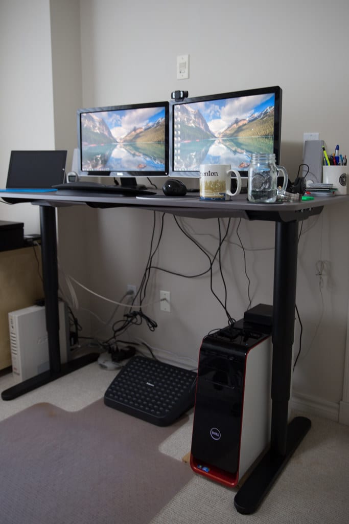A sit-stand desk raised to standing height with a monitor on an arm